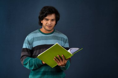 Young happy man holding and posing with the book on background.