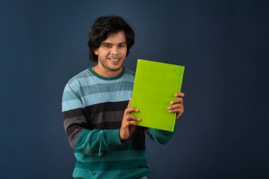 Young happy man holding and posing with the book on background.