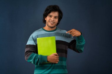 Young happy man holding and posing with the book on background.