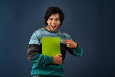 Young happy man holding and posing with the book on background.