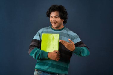 Young happy man holding and posing with the book on background.