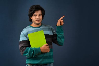 Young happy man holding and posing with the book on background.