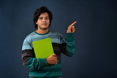Young happy man holding and posing with the book on background.