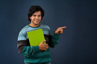 Young happy man holding and posing with the book on background.