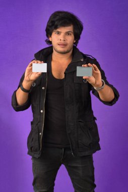 Young smiling handsome man posing with a credit card on purple background.