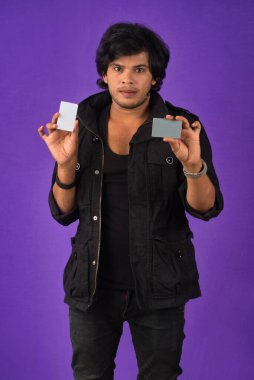 Young smiling handsome man posing with a credit card on purple background.