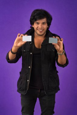Young smiling handsome man posing with a credit card on purple background.