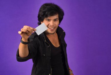 Young smiling handsome man posing with a credit card on purple background.