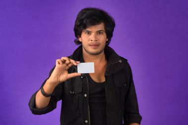 Young smiling handsome man posing with a credit card on purple background.