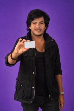 Young smiling handsome man posing with a credit card on purple background.