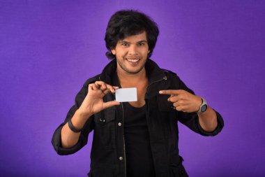 Young smiling handsome man posing with a credit card on purple background.