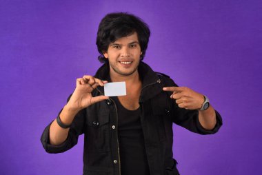 Young smiling handsome man posing with a credit card on purple background.
