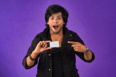 Young smiling handsome man posing with a credit card on purple background.