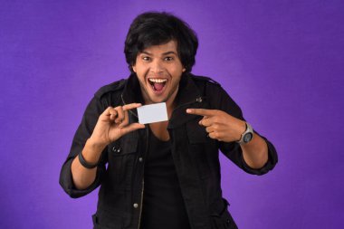 Young smiling handsome man posing with a credit card on purple background.