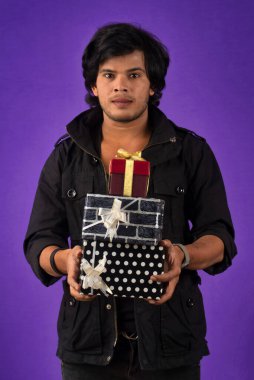 Portrait of young happy smiling handsome man holding gift box on a purple background.