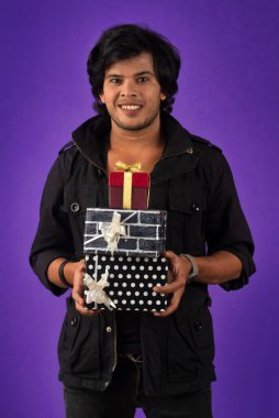Portrait of young happy smiling handsome man holding gift box on a purple background.