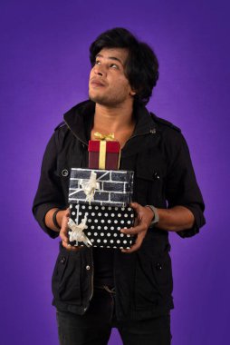 Portrait of young happy smiling handsome man holding gift box on a purple background.