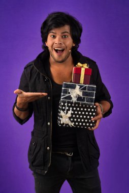 Portrait of young happy smiling handsome man holding gift box on a purple background.