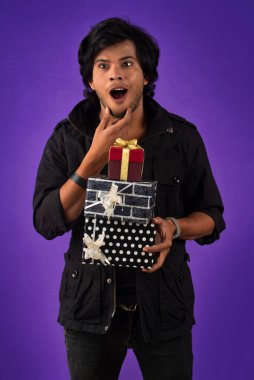 Portrait of young happy smiling handsome man holding gift box on a purple background.