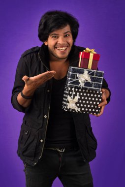 Portrait of young happy smiling handsome man holding gift box on a purple background.