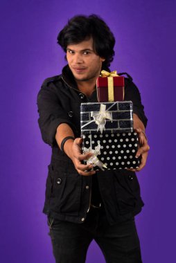 Portrait of young happy smiling handsome man holding gift box on a purple background.