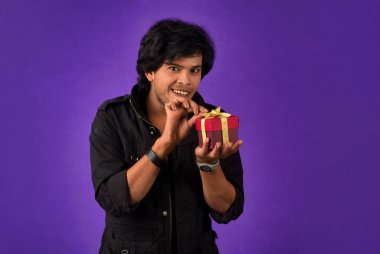 Portrait of young happy smiling handsome man holding gift box on a purple background.