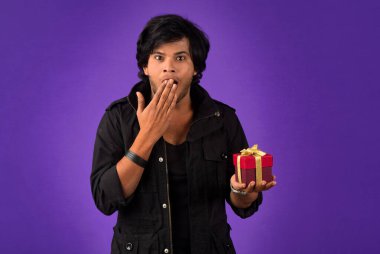 Portrait of young happy smiling handsome man holding gift box on a purple background.