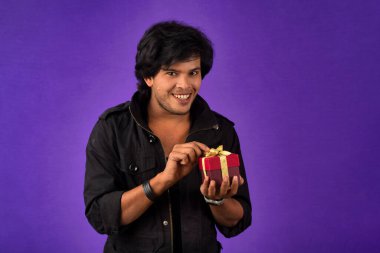 Portrait of young happy smiling handsome man holding gift box on a purple background.