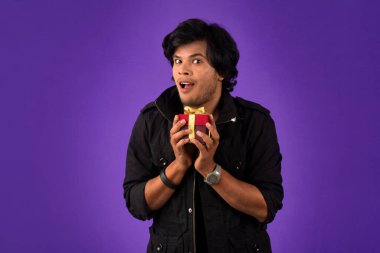 Portrait of young happy smiling handsome man holding gift box on a purple background.