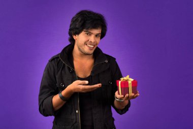 Portrait of young happy smiling handsome man holding gift box on a purple background.