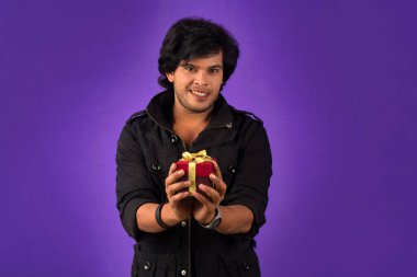 Portrait of young happy smiling handsome man holding gift box on a purple background.