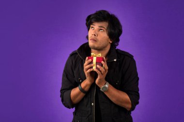 Portrait of young happy smiling handsome man holding gift box on a purple background.