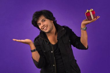 Portrait of young happy smiling handsome man holding gift box on a purple background.