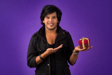 Portrait of young happy smiling handsome man holding gift box on a purple background.