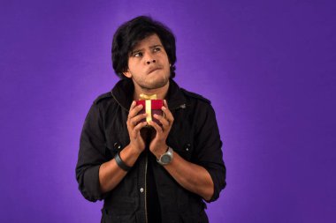 Portrait of young happy smiling handsome man holding gift box on a purple background.