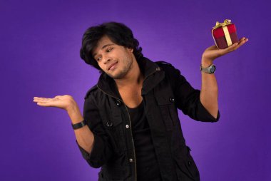 Portrait of young happy smiling handsome man holding gift box on a purple background.