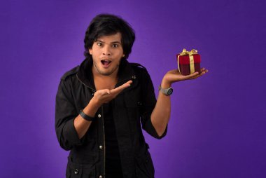 Portrait of young happy smiling handsome man holding gift box on a purple background.