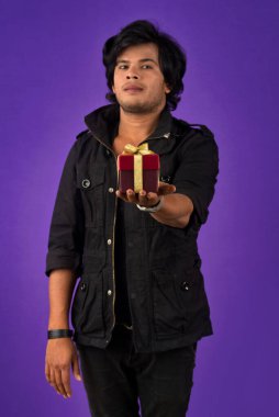 Portrait of young happy smiling handsome man holding gift box on a purple background.