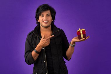 Portrait of young happy smiling handsome man holding gift box on a purple background.