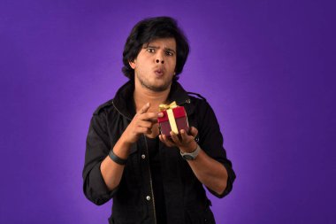 Portrait of young happy smiling handsome man holding gift box on a purple background.