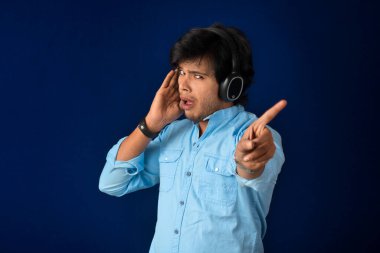 Portrait of a handsome young man enjoying music on headphones on blue background.