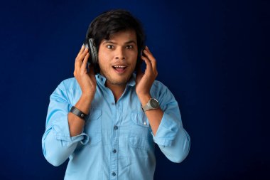 Portrait of a handsome young man enjoying music on headphones on blue background.