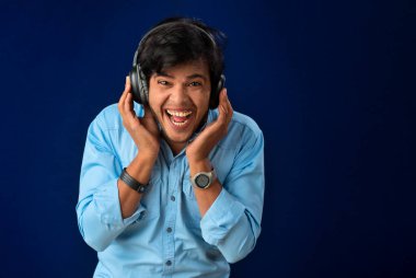Portrait of a handsome young man enjoying music on headphones on blue background.