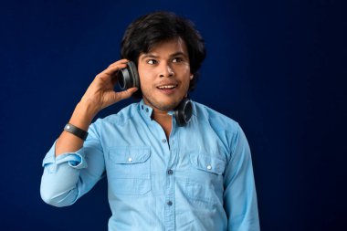 Portrait of a handsome young man enjoying music on headphones on blue background.