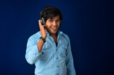 Portrait of a handsome young man enjoying music on headphones on blue background.