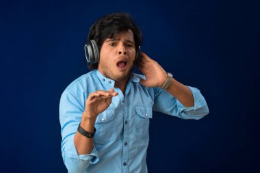 Portrait of a handsome young man enjoying music on headphones on blue background.