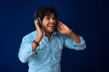 Portrait of a handsome young man enjoying music on headphones on blue background.