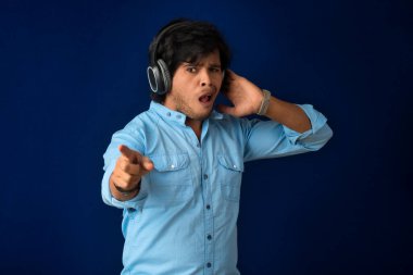 Portrait of a handsome young man enjoying music on headphones on blue background.