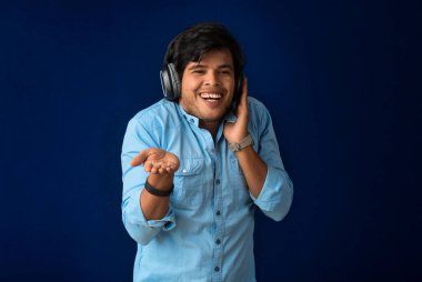 Portrait of a handsome young man enjoying music on headphones on blue background.