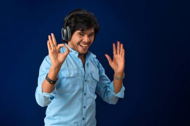 Portrait of a handsome young man enjoying music on headphones on blue background.